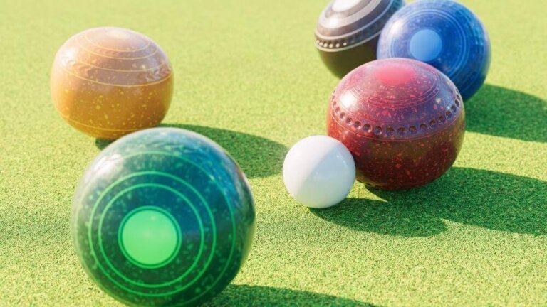 Several colourful lawn bowls and a small white jack ball are scattered on a green lawn bowling field under bright sunlight.