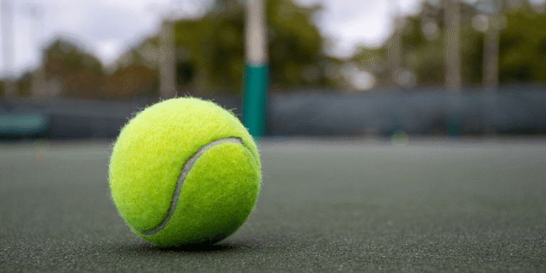 A yellow tennis ball sitting on a dark court surface.