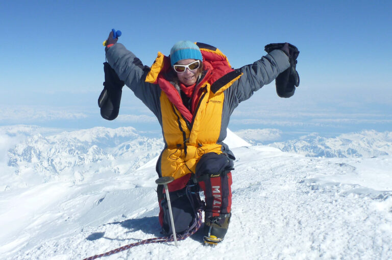 Guide Dogs Board member Katie Sarah posing with her arms up at the top of Mount Denali.