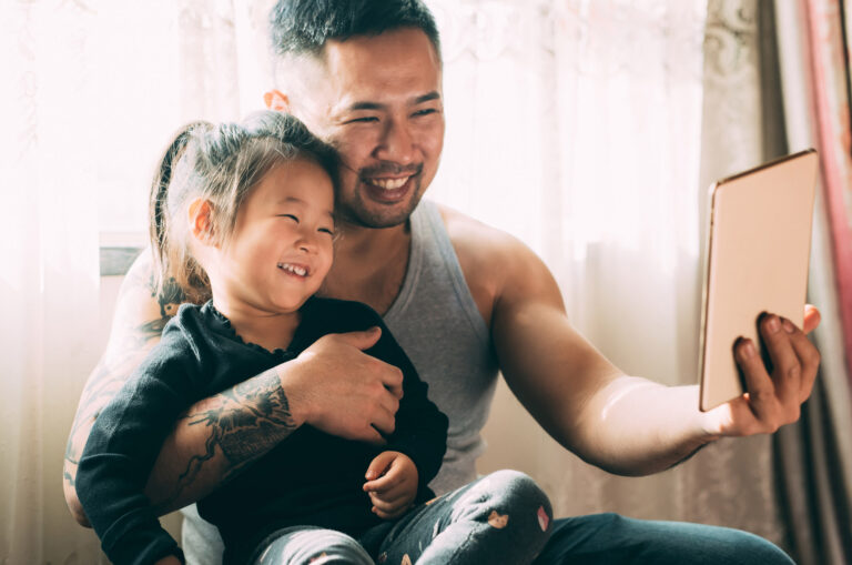 A father and young daughter are smiling and using an ipad