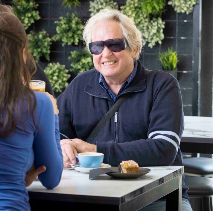 Three people seated at a cafe table. The one person who is facing the camera is smiling.