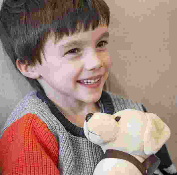 A young child on the couch cuddling up to a plush Guide Dog puppy. The child is smiling.