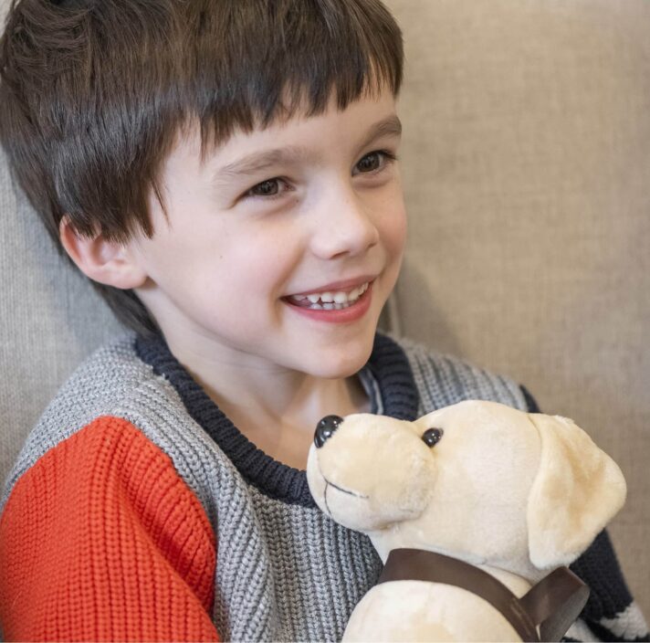 A young child on the couch cuddling up to a plush Guide Dog puppy. The child is smiling.