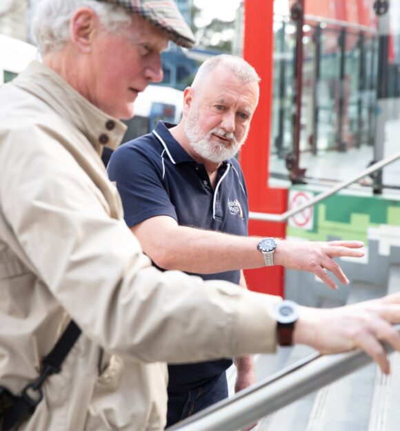 A Guide Dogs staff member assisting an an older adult with navigating a handrail.