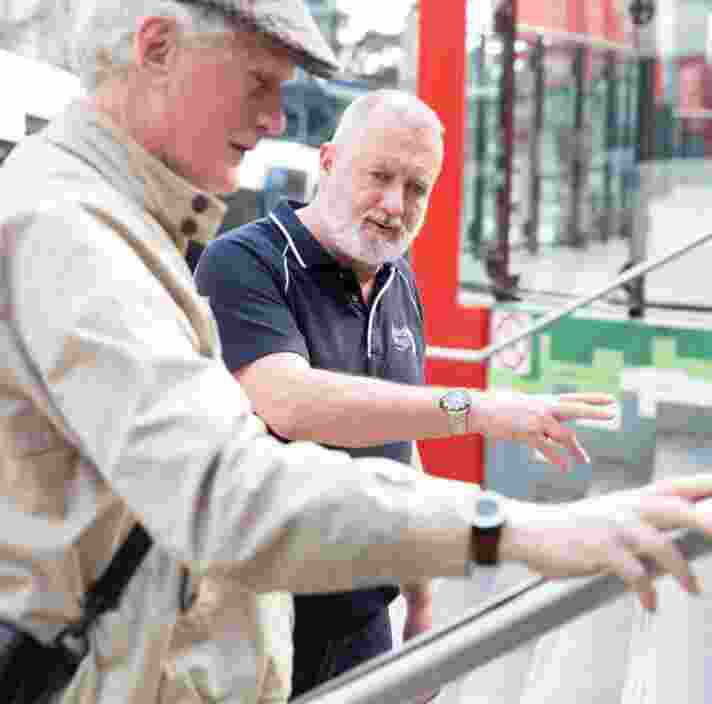 A Guide Dogs staff member assisting an an older adult with navigating a handrail.