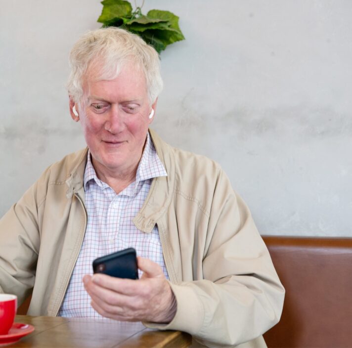 An older adult man sitting at a cafe looking at their phone.