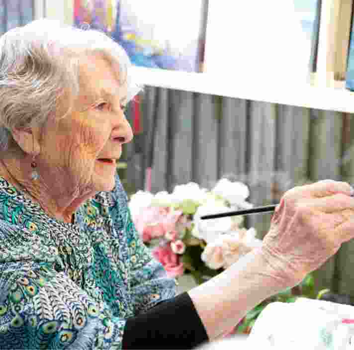 An older adult person painting with a paint brush.
