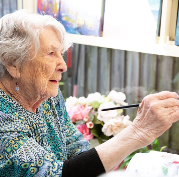 An older adult person painting with a paint brush.