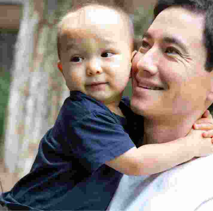 A father holding his toddler. The father has a smile on his face