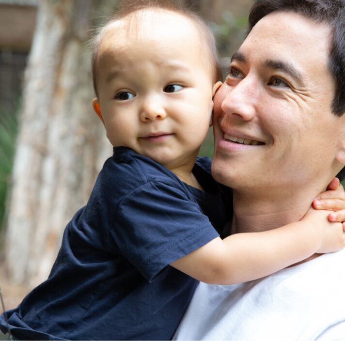 A father holding his toddler. The father has a smile on his face