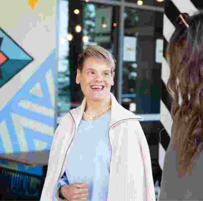 Two people looking at each other while they are walking down the street. One has their back to the camera while the other is smiling