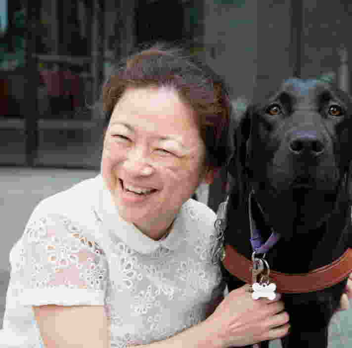 A person smiling and hugging a black Labrador dog.