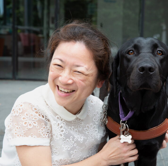 A person smiling and hugging a black Labrador dog.