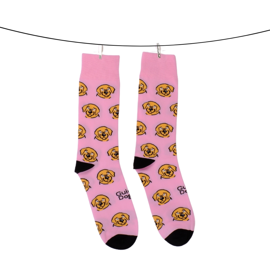 Two socks, adorned with yellow dog face patterns against a pink background, are hanging on a line secured by clothespins.