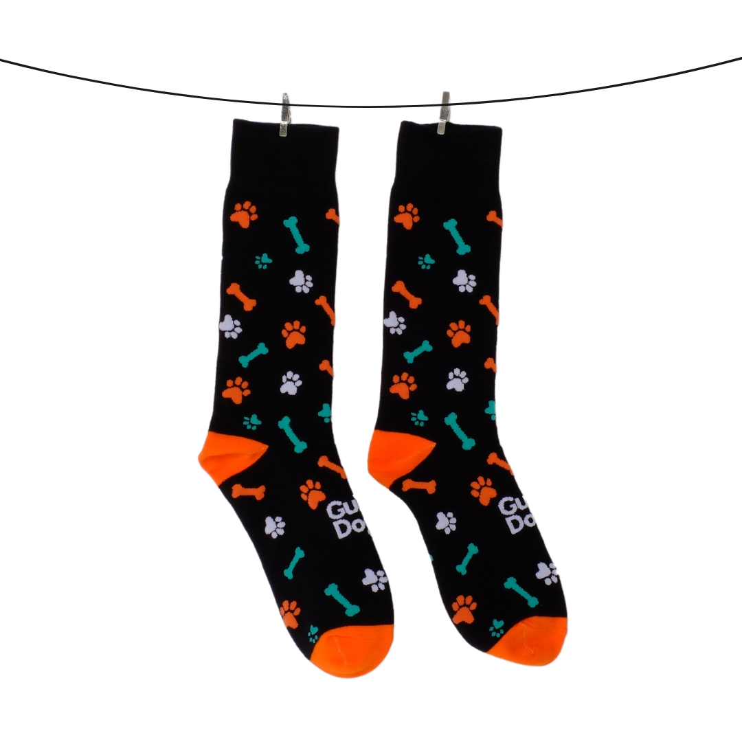 Two socks in black with orange toes and heels, showcasing a design of paws and bones, suspended on a line with clips.