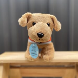 A small Plush Dog - Standing, complete with a blue tag, is positioned on a wooden stand against a gray background.