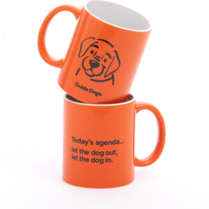 Two stacked orange mugs. The top mug shows a dogs face with the words Guide Dogs. The bottom mug reads Todays agenda... let the dog out, let the dog in.