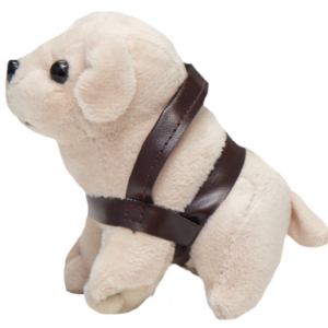 The Mini Plush Dog, wearing a brown harness, is sitting on a white surface.