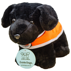 Plush black dog wearing an orange vest with a Guide Dogs tag hanging from its collar.