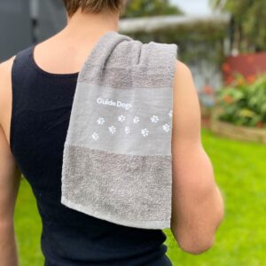 A person wearing a black tank top with a gray Pawfit Towel over their shoulder, standing outdoors.