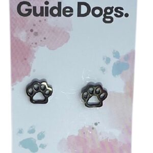 The image shows a silver paw-shaped earring on a card that reads "Proudly supporting Guide Dogs." The card has a pastel background with pink and blue splotches and small paw print designs. At the bottom, it states, "Handcrafted & made from stainless steel."