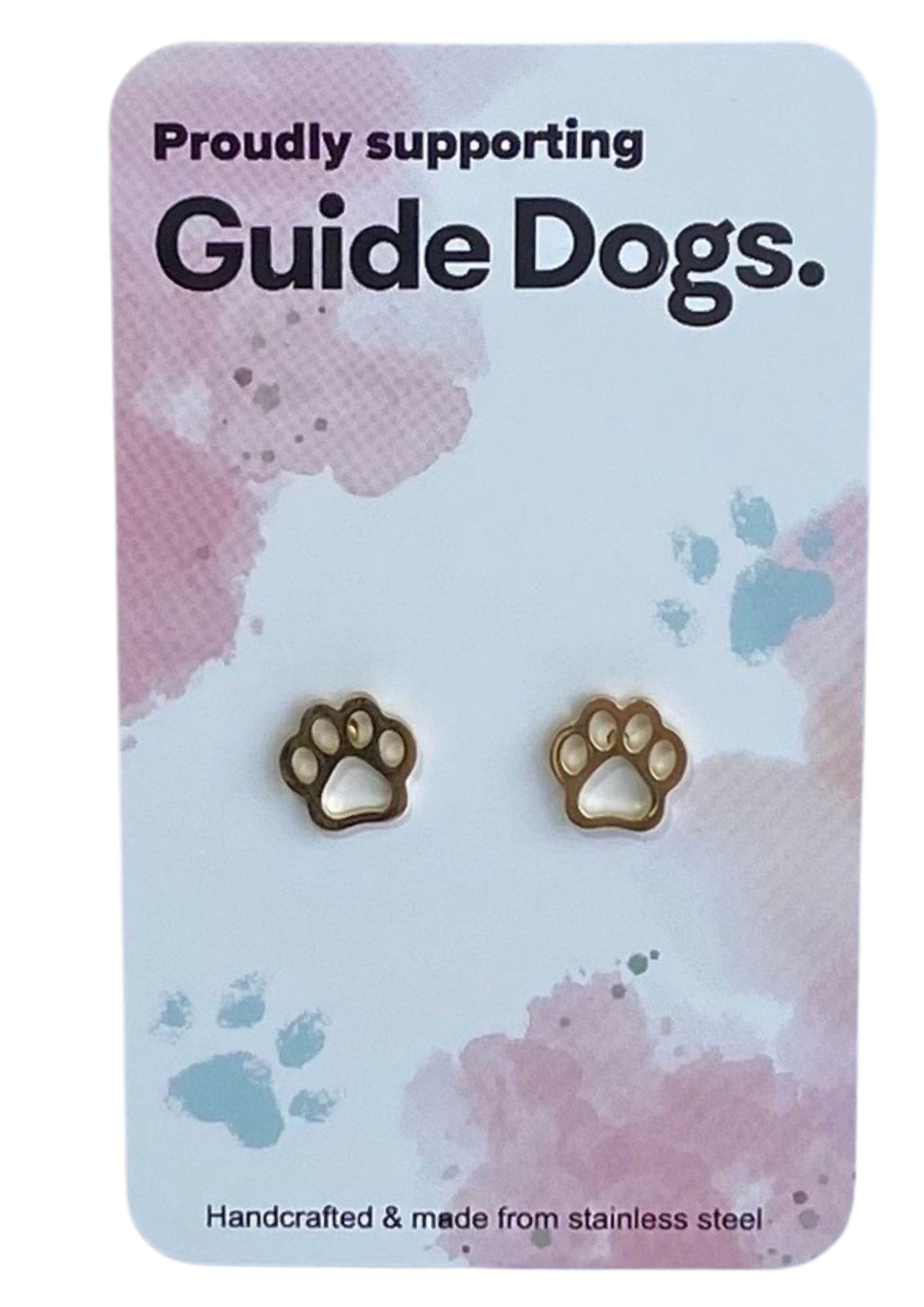 The image shows a gold paw-shaped earring on a card that reads "Proudly supporting Guide Dogs." The card has a pastel background with pink and blue splotches and small paw print designs. At the bottom, it states, "Handcrafted & made from stainless steel."