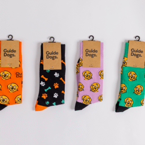 Four pairs of Socks - Coloured, featuring dog and paw print designs, are displayed side by side with Guide Dogs labels on cardboard tags.