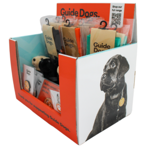 Guide Dogs Fundraising Pack: A display box with guide dog merchandise, like toys and stickers, featuring a black labrador photo and a QR code to view the full range.