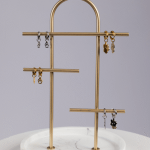 A gold and marble jewelry stand displays pairs of small gold and silver Huggie Paws earrings with various charm shapes against a light gray background.