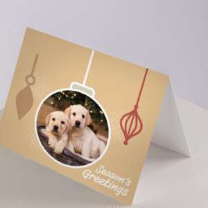 Christmas Cards - Puppies: Features two Labrador puppies inside a bauble with Seasons Greetings and ornament designs on a beige background.