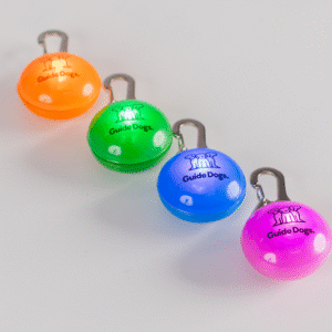 Four Clip on LED Lights in orange, green, blue, and pink, each labeled Guide Dogs with a dog logo, are arranged diagonally on a white surface.