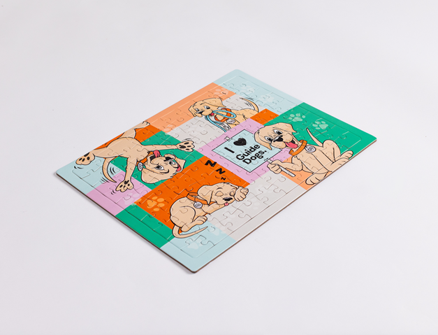 The Jigsaw Puzzle is a completed rectangular puzzle showing cartoon guide dogs in various poses with a central I love Guide Dogs sign on a colorful background.