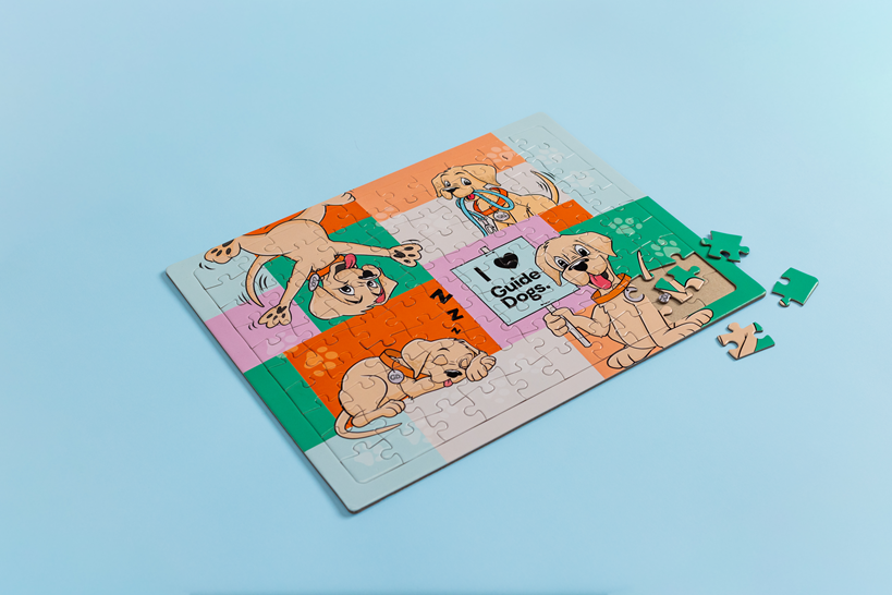 A partially completed Jigsaw Puzzle with cartoon puppies and I ♥ Guide Dogs text on a light blue background. Four pieces are beside the puzzle.