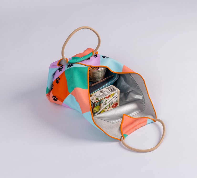 Open Lunch Bag with geometric and paw print design, holding a small food container and a juice box, displayed on a white background.