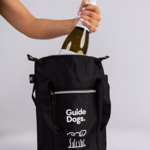 A person puts a wine bottle into a Wine Cooler Bag, which is black and labeled Guide Dogs.