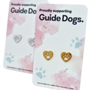 Two pairs of Earrings - Heart, one gold and one silver, featuring paw prints, displayed on Proudly supporting Guide Dogs cards with pastel paw print designs.