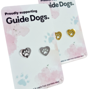 Two display cards featuring stainless steel heart-shaped earrings in silver and gold, labeled Proudly supporting Guide Dogs.